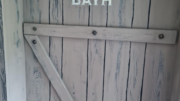 Een houten deur met de inscriptie "BATH" erboven. De deur heeft rustieke details en is in een lichte kleurtoon gehouden.
