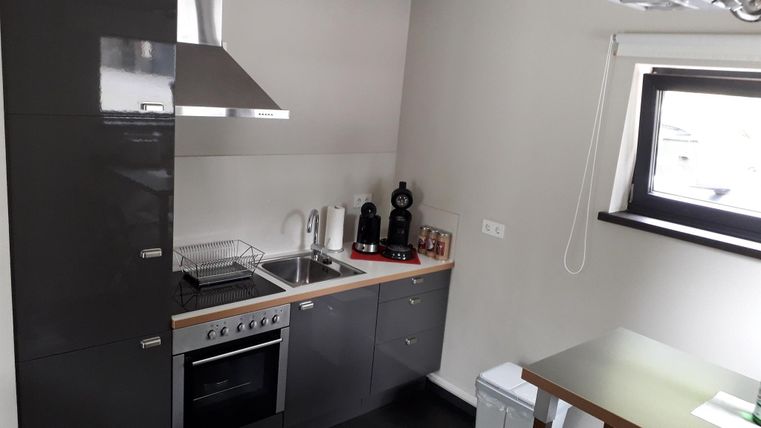 Eine moderne Küche mit grauen Schränken und Edelstahlgeräten. Es gibt einen Herd, eine Spüle und eine kleine Essgelegenheit.