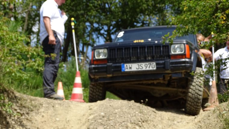 Ein Geländewagen fährt über einen unebenen Weg. Eine Person beobachtet die Situation aufmerksam.