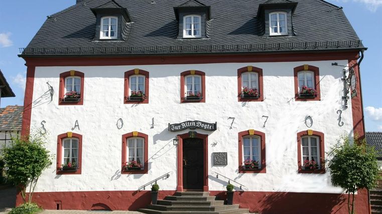 A historic house with red and white paint. The building has large windows with flower boxes and a prominent entrance door.