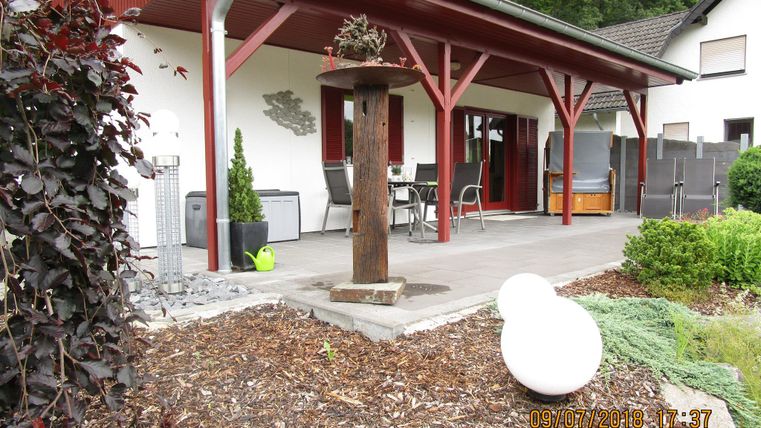 Un espace extérieur confortable avec un coin salon couvert et des meubles modernes. Le jardin est décoré avec des éléments décoratifs et une petite plante.