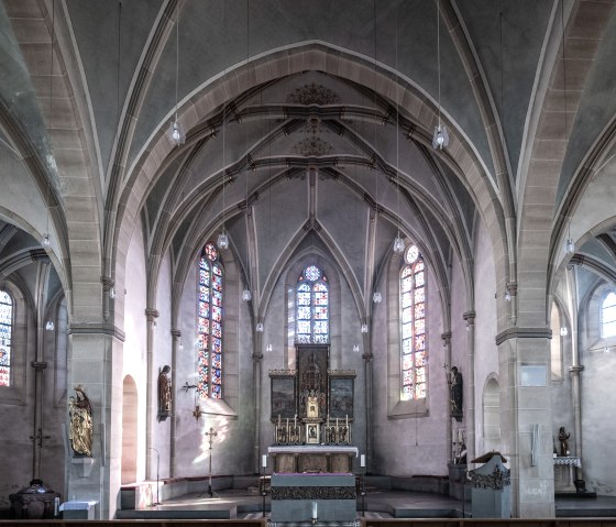 Innenansicht einer Kirche in Adenau mit gotischen Bögen, bunten Glasfenstern und einem Altar im Zentrum., © Eifel Tourismus GmbH, Dominik Ketz