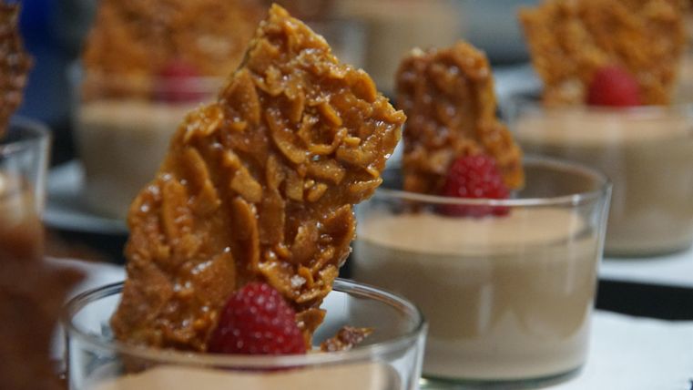 Un délicieux dessert en verrines avec une couche crémeuse et des morceaux croustillants caramélisés. Chaque portion est décorée d'une framboise fraîche.