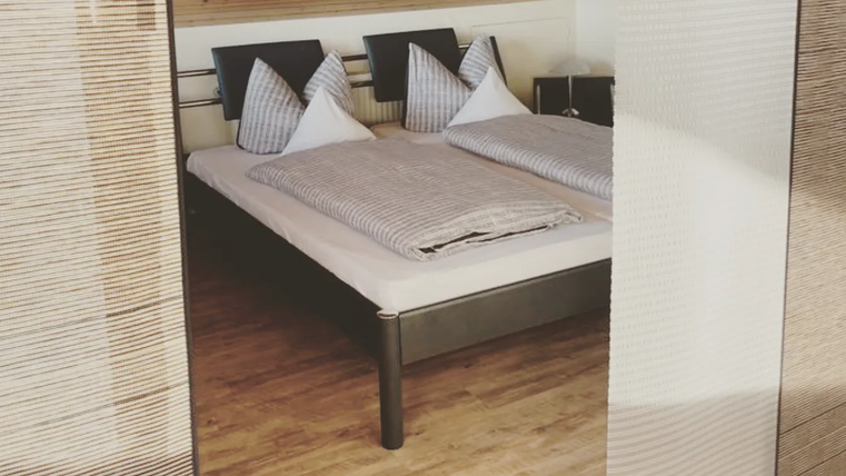 A cozy bedroom with a double bed and two large pillows. The wooden floor and warm colors create an inviting atmosphere.