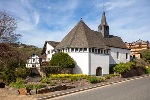 Eine charmante Kirche mit einem spitzen Turm und einer weißen Fassade. Ringsherum befinden sich grüne Sträucher und Blumenbeete.
