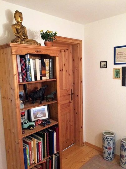 Een houten plank met boeken en decoratieve voorwerpen staat tegen een muur. Bovenop staat een Boeddha-beeld en een groene plant.