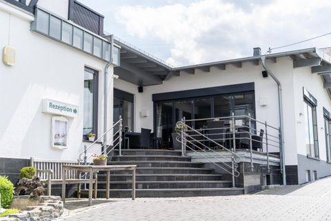 Ein modernes Gebäude mit einer Eingangstreppe und einer großen Glasfront. Draußen stehen Sitzgelegenheiten für Gäste.