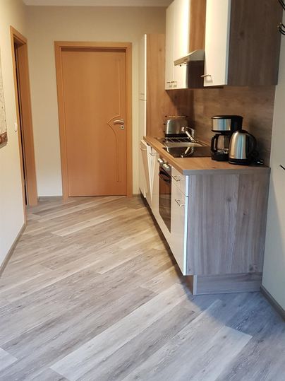 Een moderne, lichte keuken met houtlook en een aantrekkelijke werkblad. De ruimte is goed ingericht, met apparaten en een deur die naar een andere ruimte leidt.