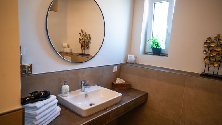 A modern bathroom with a round mirror and a sink. Fresh towels and a plant create an inviting atmosphere.
