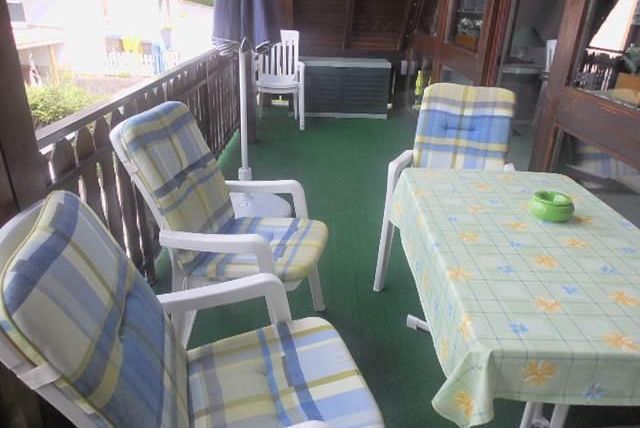 Un balcon confortable avec des chaises confortables et une table. Le sol est recouvert d'un tapis vert et l'environnement est calme.