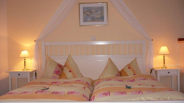 Une chambre confortable avec un grand lit double et des housses de couette claires. À côté du lit se trouvent deux tables de nuit avec des lampes.