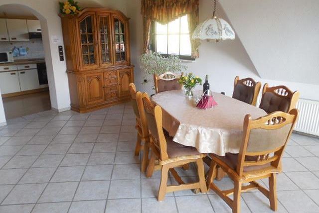 Une salle à manger accueillante avec une table ronde et des chaises. Derrière la table se trouve une belle vitrine en bois et des fleurs fraîches décorent le centre de la table.