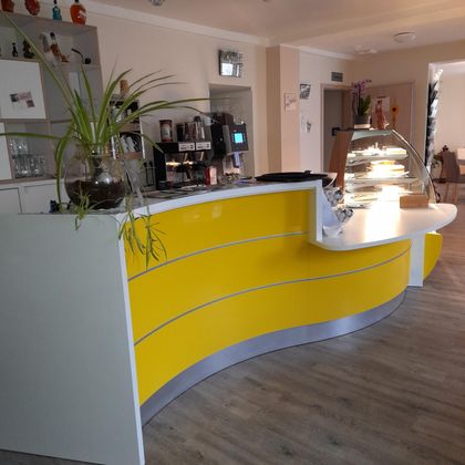 A modern reception desk in bright yellow with a striking shape. In the background, vending machines and a display case for snacks are visible.