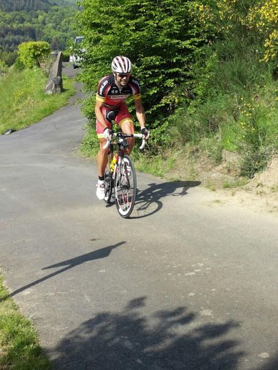 Ein Radfahrer fährt auf einem schmalen Weg durch eine grüne Landschaft. Die Sonne scheint und die Umgebung wirkt einladend.