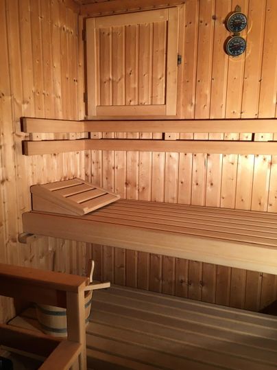 A quiet room with wood-paneled walls that represents a sauna. There are wooden benches and some thermometers on the wall.