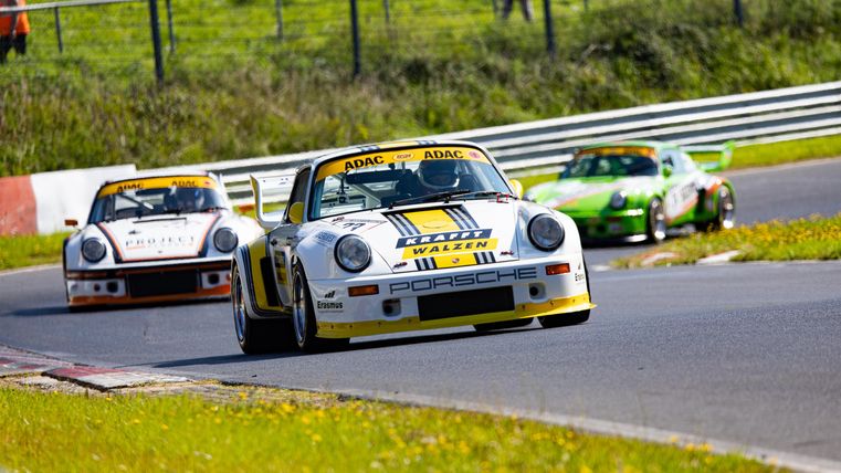 Rennwagen fahren auf einer Rennstrecke. Im Vordergrund ist ein Fahrzeug mit auffälliger Lackierung, während andere Fahrzeuge im Hintergrund sichtbar sind.