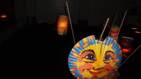 Ein farbenfrohes Laterne mit einem sonnigen Gesicht. Im Hintergrund sind schemenhaft weitere Lichter zu sehen.