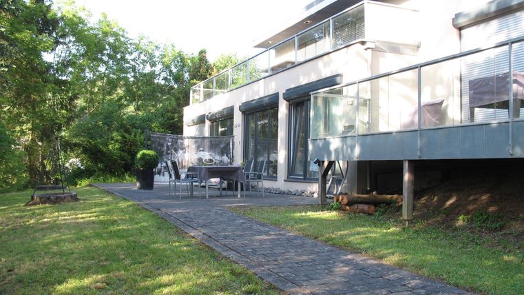 Ein modernes Haus mit einer großzügigen Terrasse und Garten. Die Umgebung ist grün und einladend.