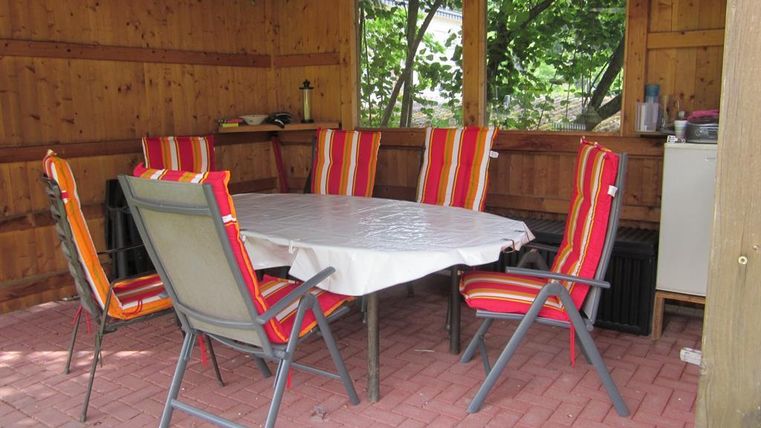 Een gezellige tuintafel met kleurrijke stoelen staat in een houten paviljoen. De ruimte heeft een warme sfeer en biedt plaats voor sociale bijeenkomsten.
