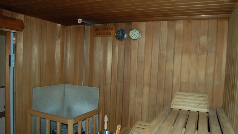 Een houten sauna met een bank om op te zitten en een watertank. Aan de muur hangen klokken voor het bijhouden van de tijd.