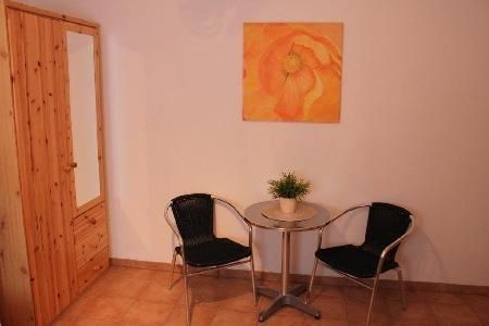 A small interior area with two chairs and a table. An orange painting hangs on the wall and a plant is on the table.