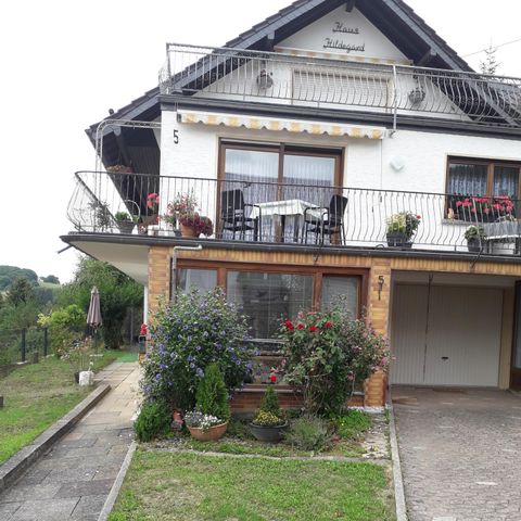A cozy house with a balcony and blooming plants. The garden is green and inviting, perfect for relaxation.