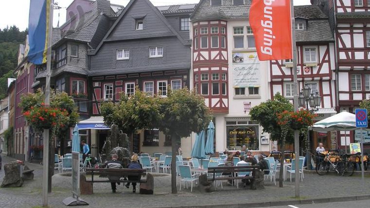 Een gezellig café met blauwe stoelen en tafels in een historische stad. Omgeven door kleurrijke bloemen en traditionele vakwerkhuizen.