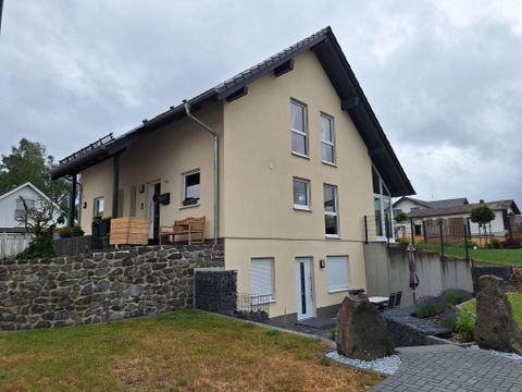 Une maison moderne avec une façade jaune et un toit en pente. Le jardin a une pelouse bien entretenue et des allées en pierre.