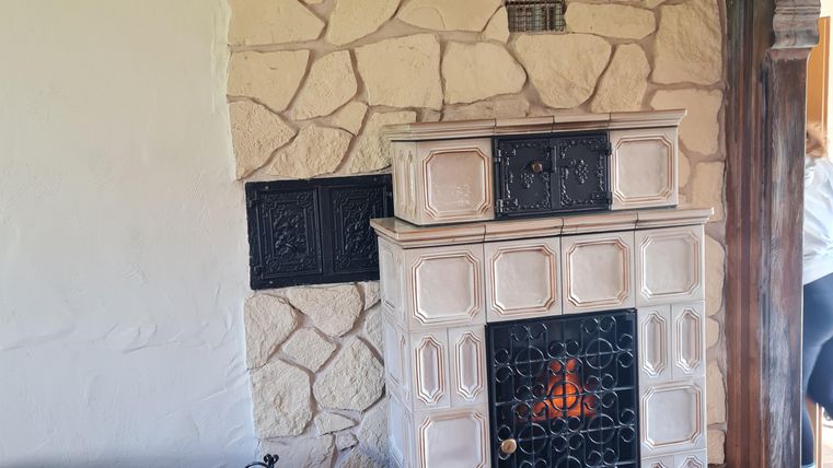 Een gezellige ruimte met een traditionele tegelkachel en een bruine leren bank. Aan de wand zijn lichte steenbekleding te zien.