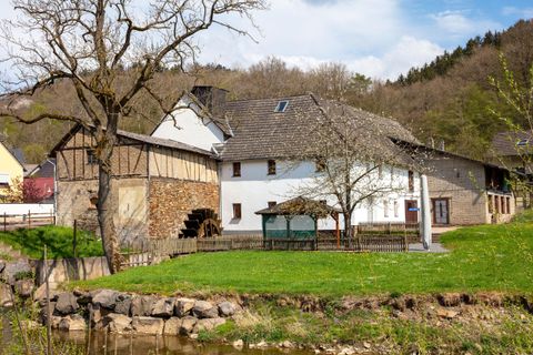 Ein charmantes, altes Bauernhaus mit einem Steinfundament und einem modernen Anbau. Umgeben von grünem Rasen und Bäumen.