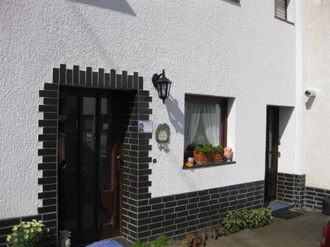 Ein Haus mit zwei Eingängen und einer weißen Fassade. Der Fensterbereich ist mit Pflanzen dekoriert.