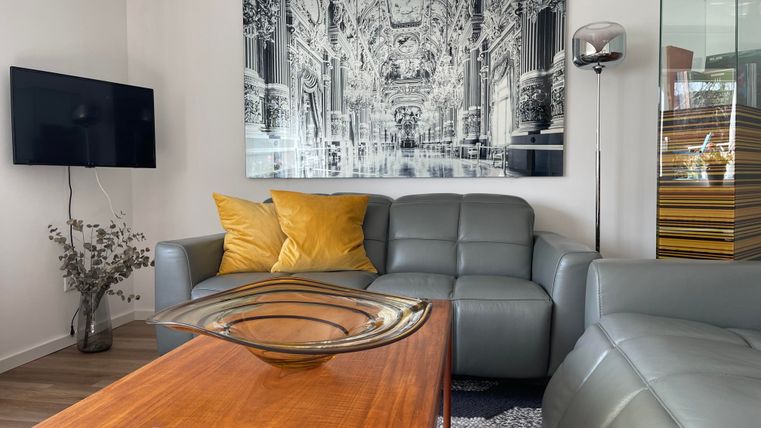 Un salon moderne avec un canapé gris et des coussins jaunes. Un impressionnant tableau en noir et blanc est accroché au mur, tandis qu'une table en bois se trouve au premier plan.