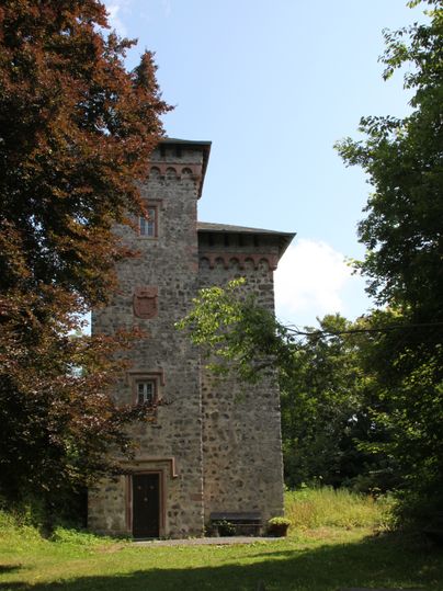Ein Steinturm mit Zinnen, umgeben von Bäumen und einer Wiese.