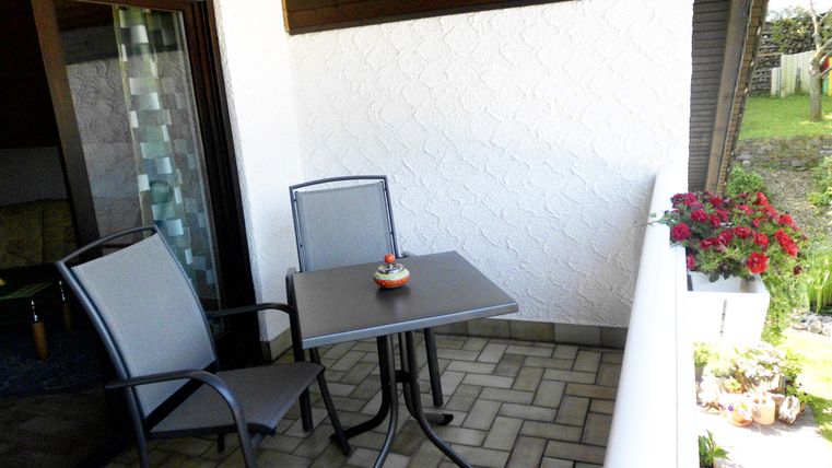 Ein kleiner Balkon mit einem Tisch und zwei Stühlen. Blühende Pflanzen schmücken die Umgebung und schaffen eine gemütliche Atmosphäre.