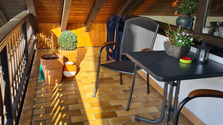 A cozy balcony with a table and chairs. Plant pots and decorative plants create an inviting atmosphere.