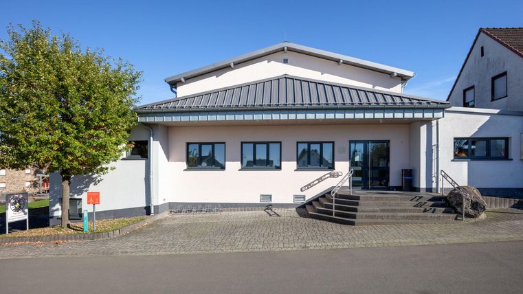 Ein modernes Gebäude mit einem flachen Dach. Der Eingangsbereich ist mit Treppen und großen Fenstern gestaltet.