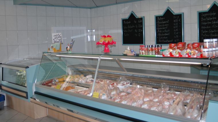 Eine Fleischtheke in einem Geschäft mit verschiedenen Fleischsorten und Kühlregalen. Im Hintergrund sind Tafelaufschriften und Produkte zu sehen.