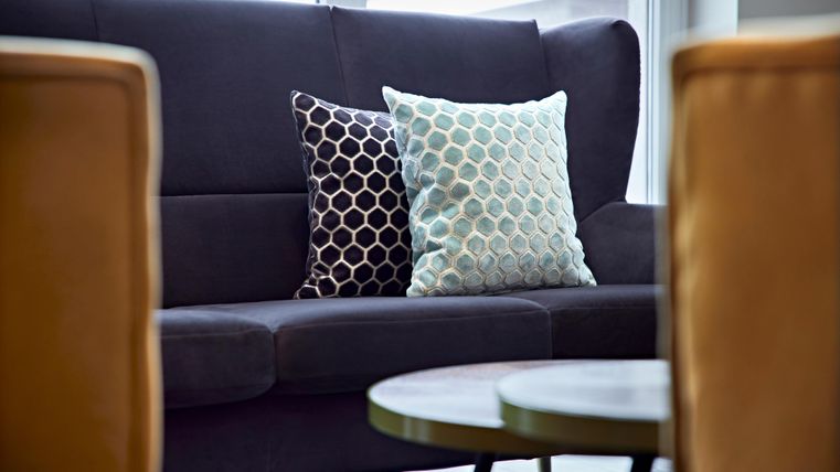 A modern living room with a comfortable sofa and two decorative cushions. In the foreground are two small tables.
