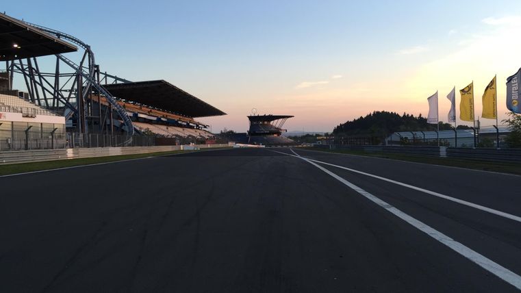 Eine Rennstrecke mit dem Blick auf die Tribünen bei Sonnenuntergang. Der Himmel ist blau und die Atmosphäre ist ruhig.