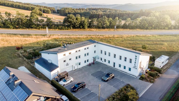 Een modern gebouw met meerdere voertuigen op een parkeerplaats. Omgeven door groene landschap en een heldere lucht.
