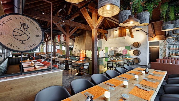 A modern restaurant with rustic wood decor. The large table is beautifully set, and in the background, you can see cooking and dining areas.