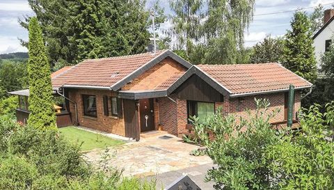 A cozy single-family brick house with a red roof. The house is surrounded by green trees and bushes.