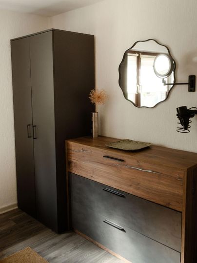 Ein modern eingerichteter Raum mit einem Holzsideboard und einem schwarzen Schrank. An der Wand hängt ein runder Spiegel.