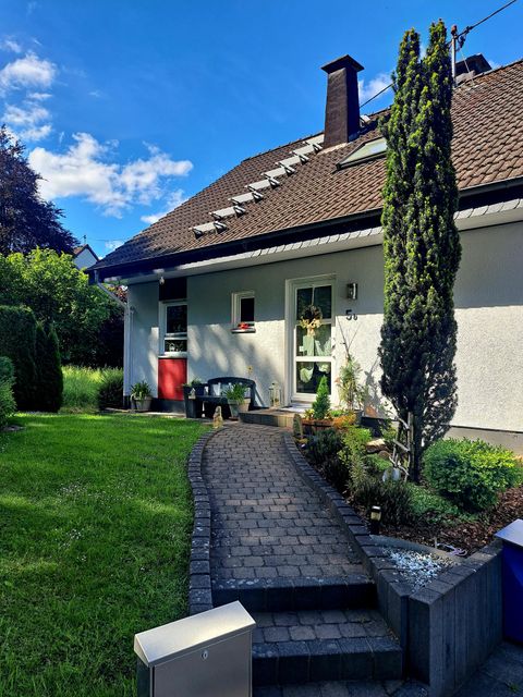 A modern house with a well-kept garden. The paved walkway leads to the front door, surrounded by green plants.