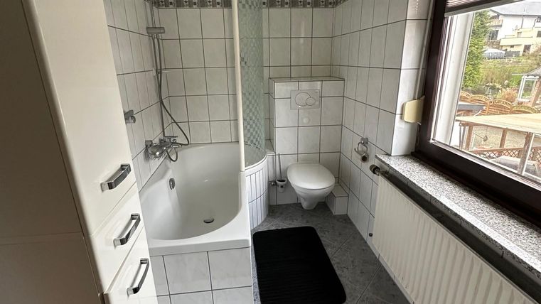 Een moderne badkamer met een douche en een bad. De muren zijn betegeld en er is natuurlijke verlichting door een raam.