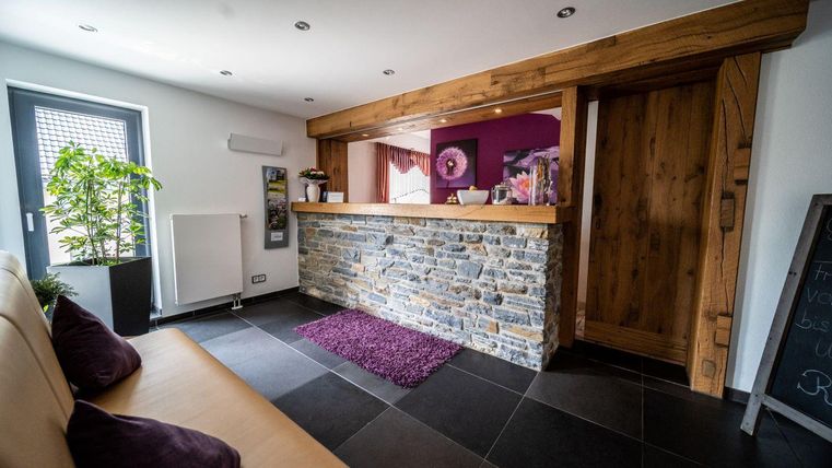 Een moderne ontvangstruimte met een houten en stenen paal. De zithoek is uitnodigend en versierd met een plant.