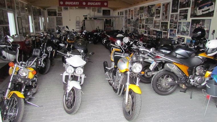 A large collection of motorcycles is in a garage. The walls are decorated with photos and posters.