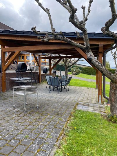 Een gezellige buitenruimte met een overdekte tafel en stoelen. Op de achtergrond zijn weilanden en bomen te zien.