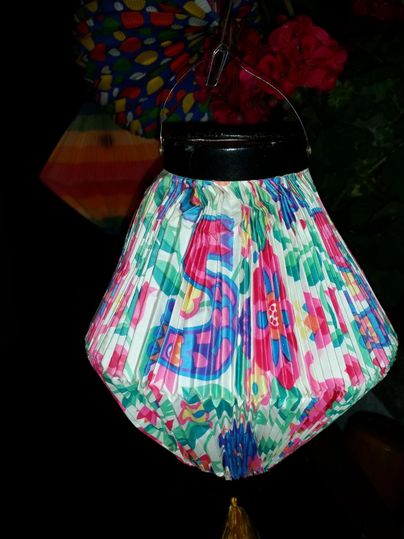 Eine bunte Laterne mit einem floralen Muster hängt an einem Haken. Im Hintergrund sind weitere farbenfrohe Dekorationen sichtbar.