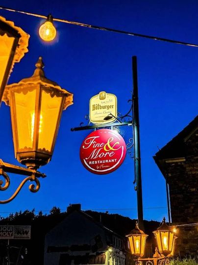 Une enseigne de restaurant la nuit avec une lumière chaude provenant des lanternes. Le ciel est bleu foncé et crée une ambiance accueillante.